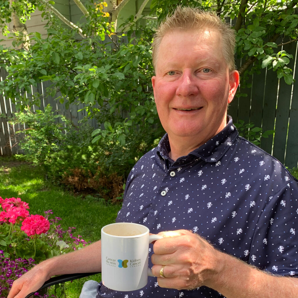 Russell Barnes Man in blue and white shirt sitting in yard and holding a coffee mug with Kidney Cancer Canada logo on it - Russell Barnes.
