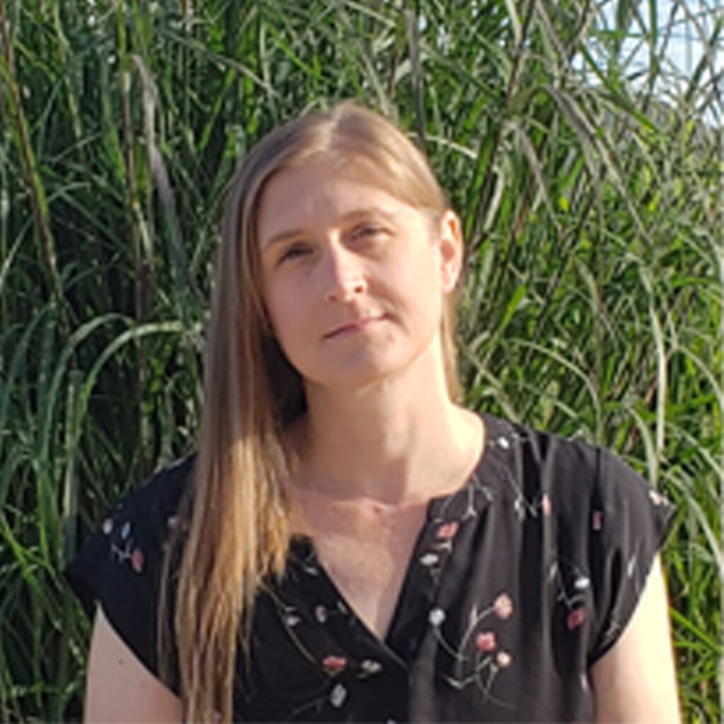 Christine Golding woman in black shirt with flowers on it and tall grass in the background - Christine Golding.