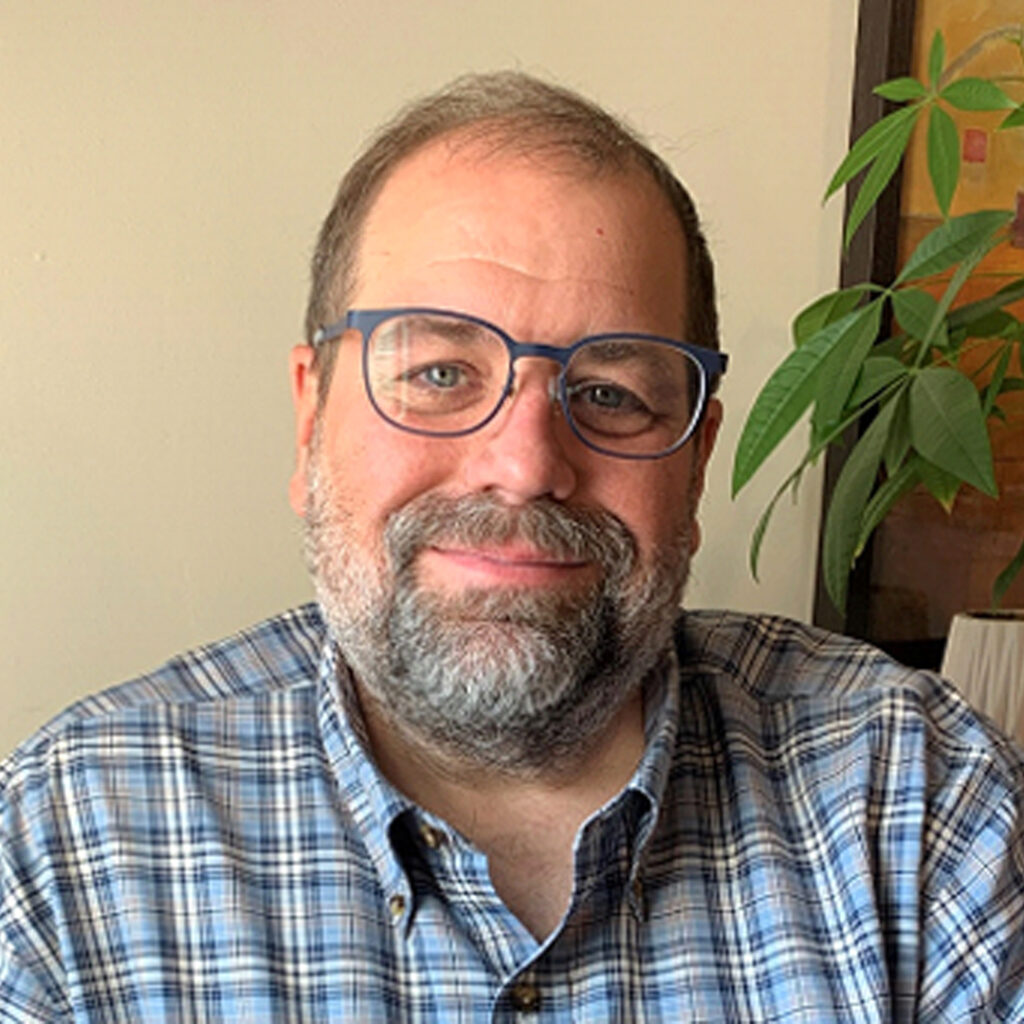 Ed Faddies Man in striped blue and white shirt sitting next to plant - Ed Faddies.